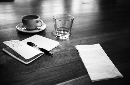 A photograph of a cup of coffee with a notebook and pen.